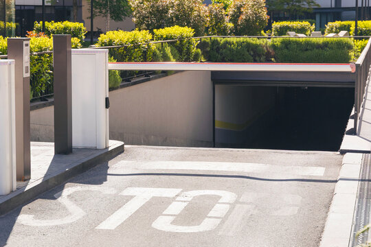 Boom barrier closing access to an underground parking garage with a STOP sign painted on the asphalt. Urban security and access control concept