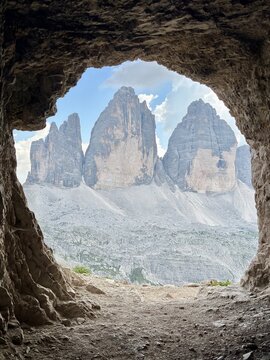 Iconic Tre Cime di Lavaredo mountain peaks framed by a dark cave entrance in the Dolomites, Italy. Dramatic view of the famous alpine landmark on a popular hiking route.