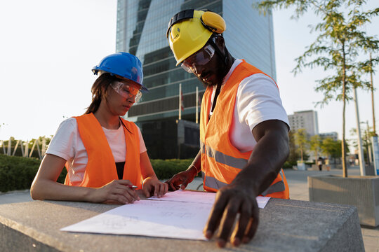 Diverse engineers collaborating on construction plans outdoors in city