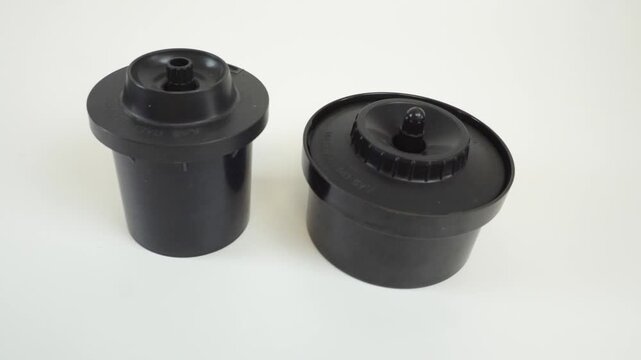 Two black film developing tanks for analog photography. Soviet darkroom equipment for 35mm and 120 film. Vintage plastic film processing tanks on white background.