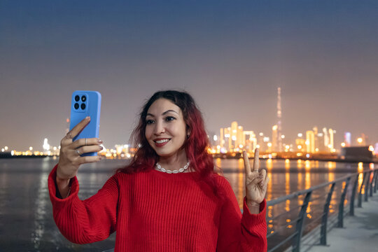 Young woman creating content, smiling and holding a smartphone, with the Dubai skyline in the background