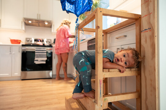 Candid toddler resting on kitchen stool while parent cooks nearby