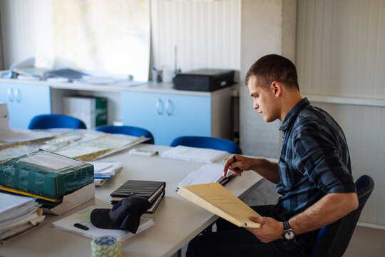 Man Working at Desk in Office Reviewing Documents and Maps