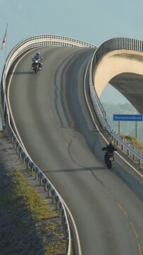 Two motorbikers ride along the Atlantic Ocean Road towards each other and greet each other.