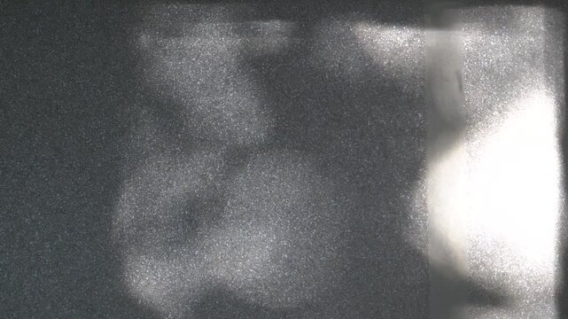 Sunbeams on the wall. Light glints and reflections on a dark surface. Abstract light spots with a grainy texture. Play of light and shadow. Optical effects.