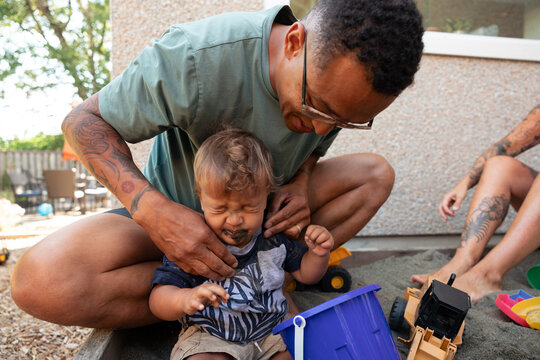 Candid moment: father comforting toddler in sandy backyard play
