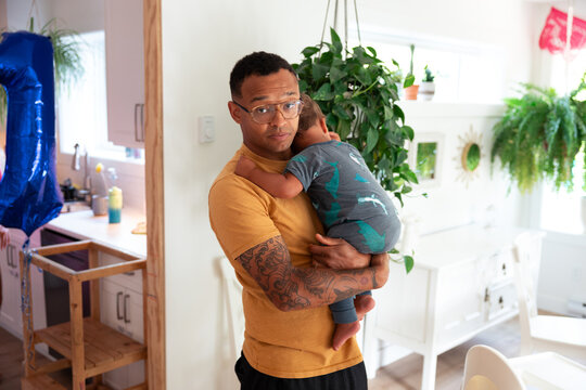 Tired dad holding sleeping child in bright home, tender family moment