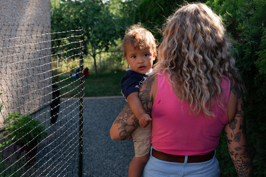 Candid mother carrying toddler with tattoos in sunny garden