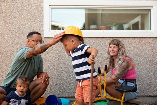 Candid family moment: dad helps son wear hard hat during play