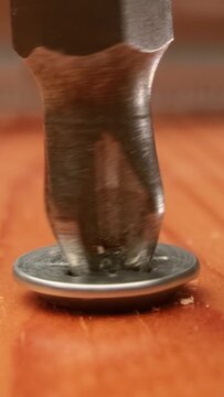 Close-up is an electric drill the screws a self-tapping screw into a wooden bar.