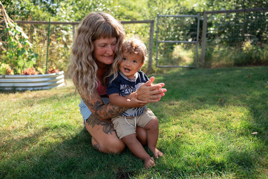 Mother playing with toddler in sunny backyard garden, candid moment