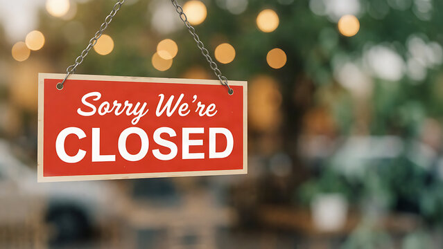 Red sorry we're closed sign hanging in a cafe window with bokeh lights