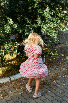 Child Twirling in a Pink Dress Among Flowers on a Sunny Day