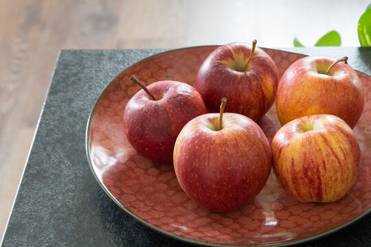 Fresh Red Apples in a Ceramic Bowl on a Kitchen Counter. Vibrant group of ripe, striped red apples beautifully arranged in a decorative bowl.