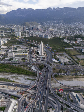 Aerial view of a complex highway interchange with heavy traffic, surrounded by modern urban buildings and the dramatic backdrop of the mountains in Monterrey, Nuevo Leon, Mexico.