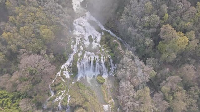 Aerial view of Marmore Falls with cascading water flowing through lush forest and rocky terrain in Terni, Umbria, Italy.