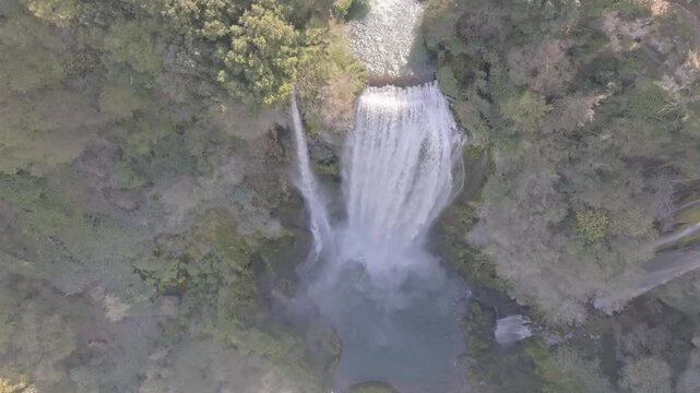 Aerial view of Marmore Falls cascading into the river surrounded by lush green forest and rocky cliffs in Terni, Umbria, Italy.
