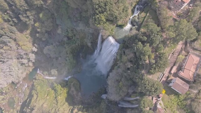 Aerial view of Marmore Falls cascading into a pool surrounded by lush green forest and rocky terrain in Terni, Umbria, Italy.