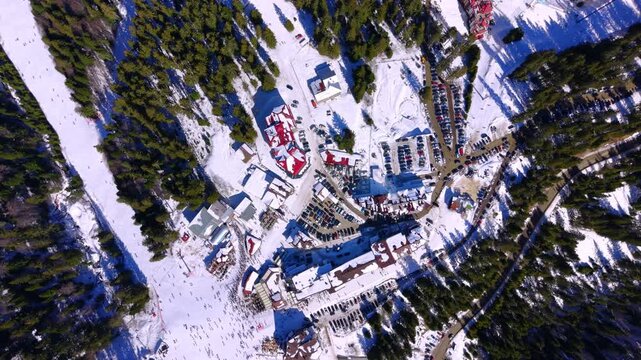 Resort base, parking lots and crowded slope, Pamporovo, Bulgaria. Snow covered hotels and restaurants, cars in several lots, lift station, spruce forest and many skiers on the run.