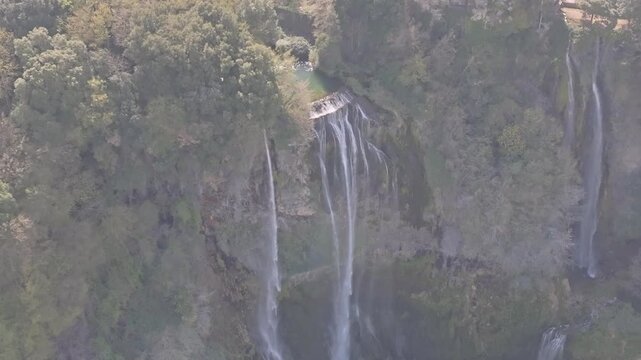 Aerial view of the cascading waters of Marmore Falls surrounded by dense green forest and rocky cliffs in Terni, Umbria, Italy.
