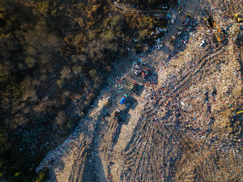 Aerial view of TPA Suwung landfill with heavy machinery, trucks, and waste piles in Kecamatan Denpasar Selatan, Bali, Indonesia.