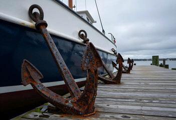Obraz premium Maritime stability and nautical heritage, rusty iron anchors resting on a wooden pier beside a docked boat for marine industry and travel concepts