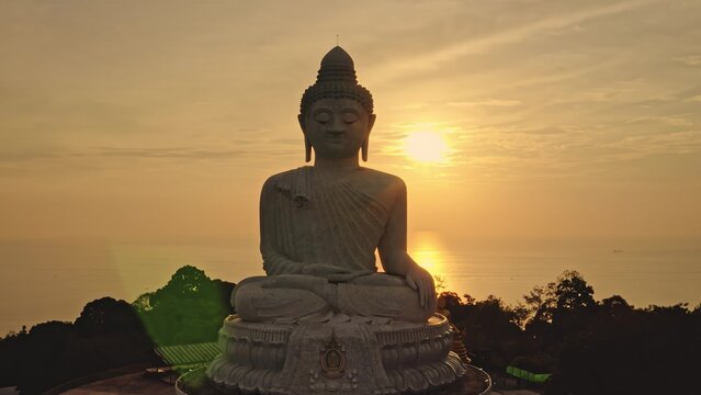 Aerial view of the Big Buddha statue illuminated by the warm golden light of the setting sun over the ocean in Phuket, Phuket, Thailand.