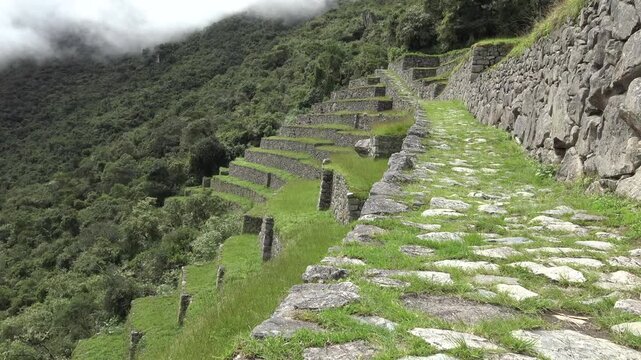 Inca agricultural terraces and stone path at Machu Picchu, Peru, with mist over the green cloud forest of the Andes