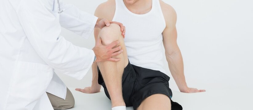 Doctor examining man's knee while sitting on treatment table