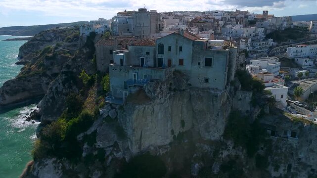 Castello di Peschici castle on cliff over marina Peschici Gargano Puglia Italy aerial orbit drone shot with upward reveal of beach background vertical rock promontory cinematic B-roll
