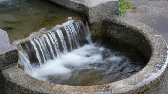 石の水盤から溢れ落ちる水 シームレスループ動画背景 16:9 4K