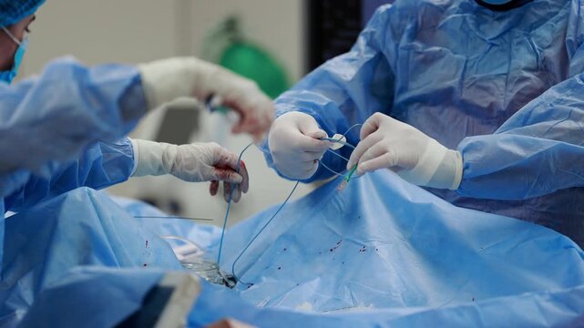 Medical team in sterile gloves preparing guidewire and catheter before cardiac catheterization, close up on blue sterile drape in cath lab