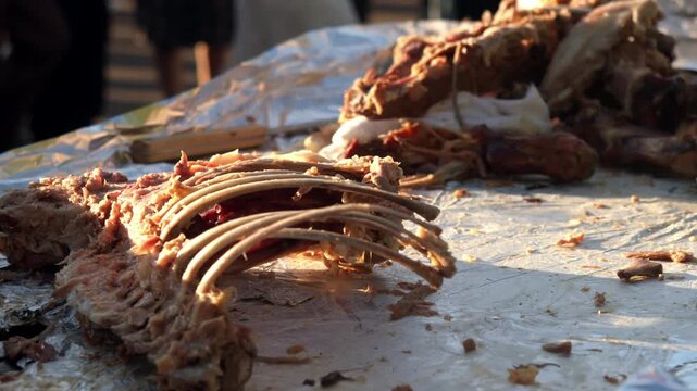 Close up shows remains of carved roasted pig resting on aluminum foil. Bare ribs and meat scraps are left after serving hungry crowd at outdoor street food festival.