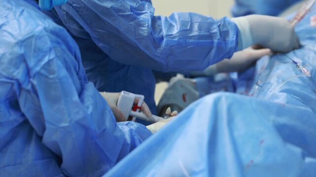 Close up of gloved hands connecting inflation syringe to catheter during balloon angioplasty, interventional cardiology procedure in hospital