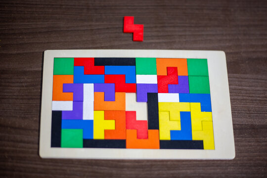 A top view of a colorful wooden pentomino puzzle board with a single red piece outside. Intellectual logical spatial training game layout. Hobbies leisure, education activity.