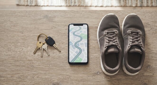 Modern smartphone with GPS map navigation route, keys, and running sneakers on a wooden table.