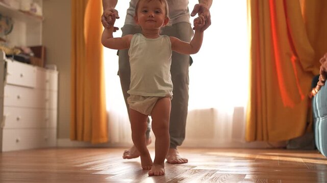 baby first steps. happy family kid dream concept. father teaches baby daughter to take first steps at home in front of window. father's day concept. lifestyle baby takes his first steps