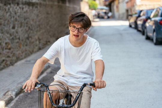 Focused teenage boy with Down syndrome riding adult tricycle independently through Spanish town