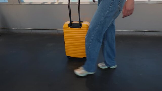 Woman Walking Luggage Suitcase Airport Corridor Motion Legs. A passenger pulling a bright yellow rolling suitcase while walking through a modern airport terminal corridor during travel