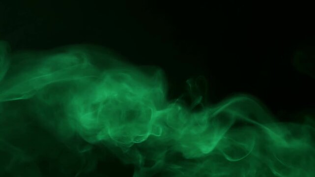Slow motion tracking of green smoke swirling across black studio background with drifting vapor patterns