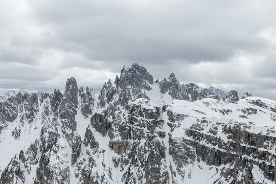 Snow covers the peaks of Tre Cime in the Dolomites during winter. The sky is cloudy, and the mountain scenery is striking.