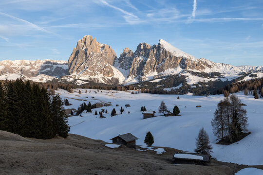 Snow covers the landscape at Alpe di Siusi in the Italian Alps at winter, showing mountain peaks and small wooden cabins.