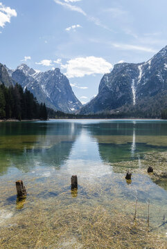 Snow covers the mountains surrounding Toblacher See, an alpine lake in the Dolomites. The water reflects the winter landscape.
