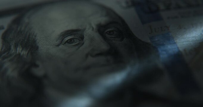 Extreme macro close-up of a hundred US dollar banknote in dark surroundings, illuminated from beneath by a scanner light. Suitable for finance, banking, currency, wealth, economy, authentication.