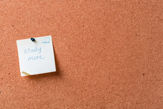 Sticky note with study more goal pinned to a textured cork board, a handwritten reminder with copy space for planning and motivation