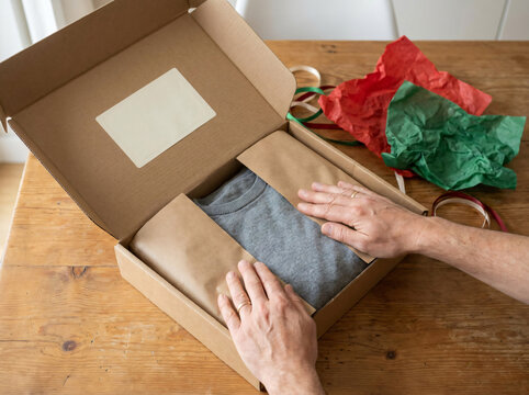 Hands packing a grey sweater into a cardboard box. Person returning a gift after Christmas.