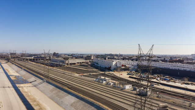 Aerial view of extensive railway tracks and industrial buildings with power lines under a clear blue sky in Los Angeles, California, United States.