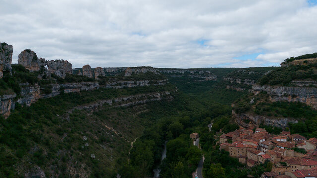 serene canyon landscape with rock formations and lush vegetation under a cloudy sky. aerial perspective of natural outdoor environment. Risco los camellos, Cascada de Orbaneja del Castillo