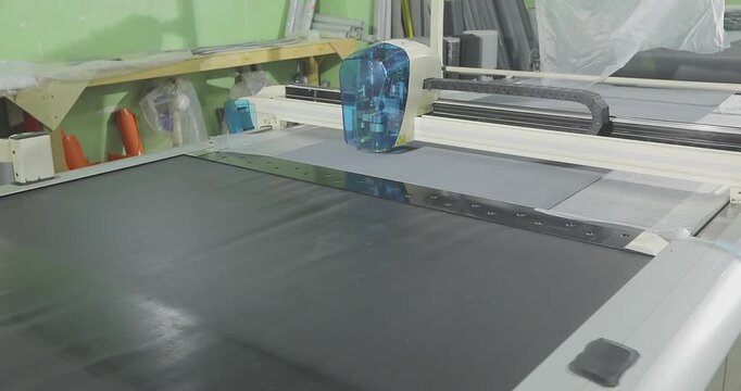 Automated cutting of grey upholstery fabric on a CNC plotter. Fabric cutting process on a CNC machine in a modern production workshop. Garment or furniture factory.
