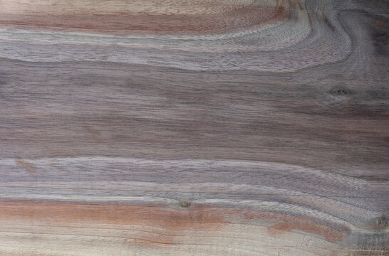 Full frame texture of polished natural walnut wood slab with a prominent tree knot and wavy grain pattern. Detailed close-up background of luxury dark wooden board